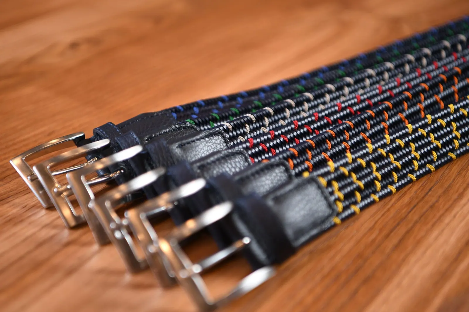 Cinture intrecciate con fili colorati, disposte una accanto all’altra su un piano di legno